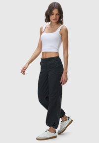 Vit kortärmad topp med fyrkantig halsringning, i kombination med svarta, löst sittande cargobyxor och vita sneakers med en ljusbrun sula.