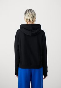 Sudadera negra con un corte relajado, que cuenta con capucha ajustable, puños acanalados y dobladillo. Combinada con pantalones de chándal azules, de textura suave.