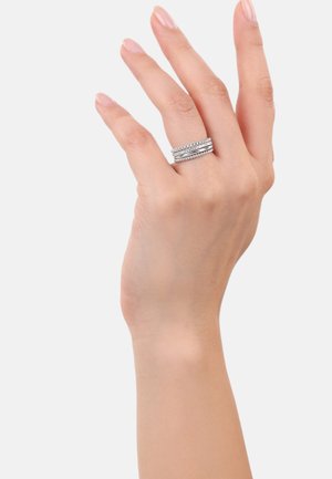 Eine Hand mit manikürten Fingern zeigt drei stapelbare Silberringe, die jeweils zarte Designs und ein poliertes Finish aufweisen.