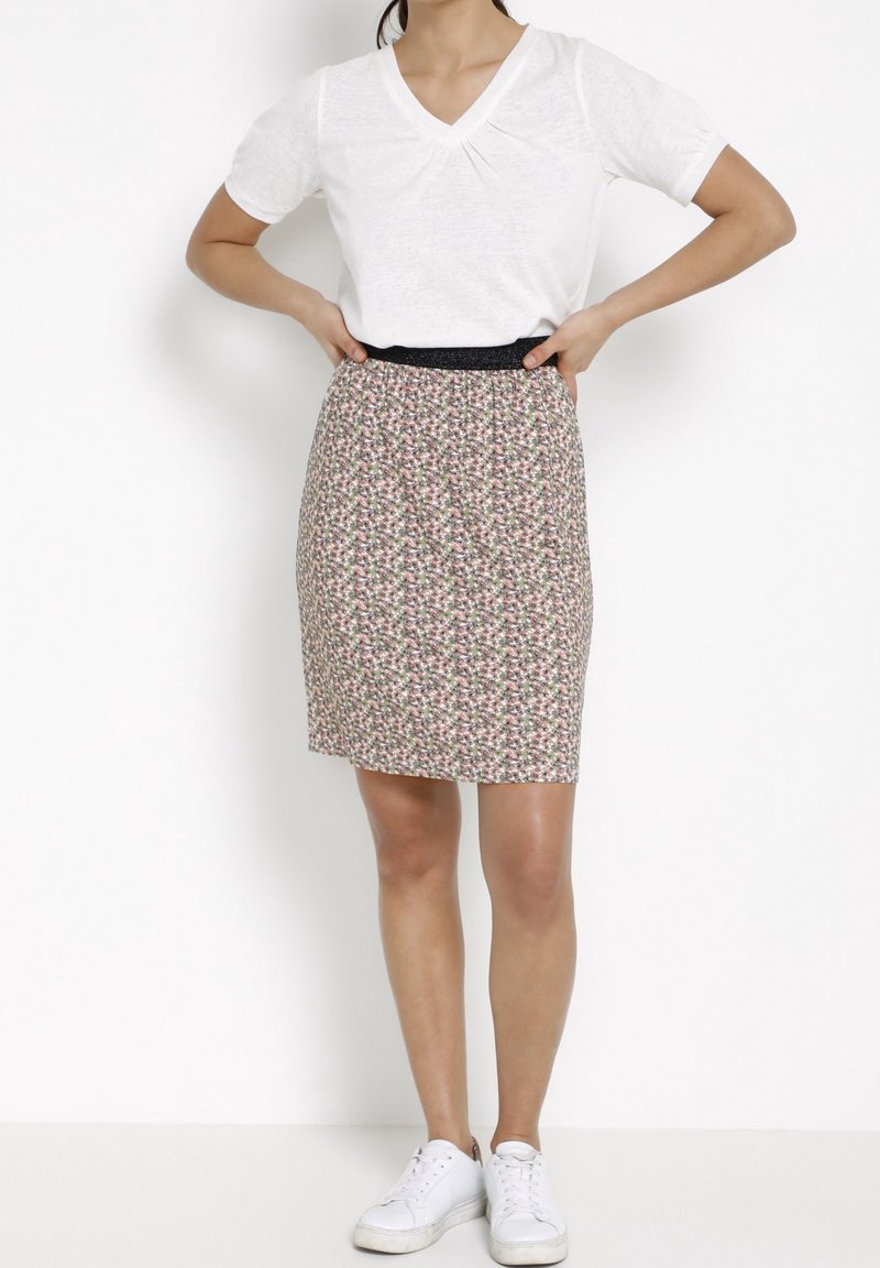 Camiseta blanca de manga corta y cuello en V combinada con una falda de longitud a la rodilla, estampada con flores, que tiene una cinturilla elástica negra y zapatillas blancas.