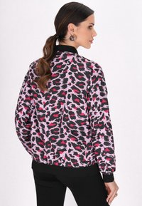 Jachetă cu model de leopard, în nuanțe de negru, roz și roșu. Realizată dintr-un material neted, cu un guler și mansete cu bandă.