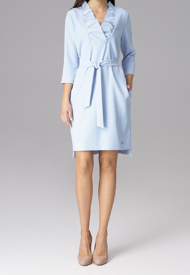 Femme portant une robe bleu clair mi-genoux avec des manches trois-quarts, un col en V à volants, une ceinture nouée à la taille et des talons hauts couleur nude.