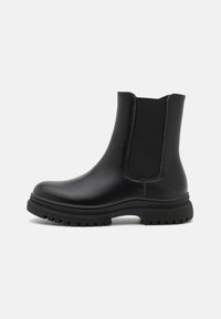 Bottine noire en cuir avec panneaux élastiques sur les côtés, bout rond et semelle épaisse à crampons. Texture lisse avec des détails de couture minimaux.