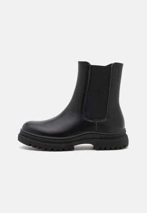Bota de tornozelo em couro preto com painéis laterais elásticos, bico arredondado e sola robusta com textura rugosa. Textura lisa com detalhes de costura mínimos.