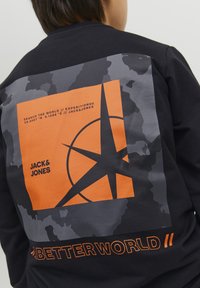 Felpa nera con una grande grafica multicolore, che include un quadrato arancione con un design a stella, testo e accenti di motivo mimetico.