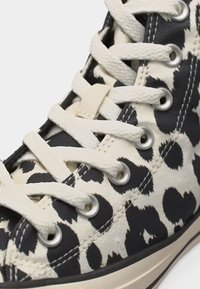 Πάνω από τον αστράγαλο αθλητικό παπούτσι με λευκά κορδόνια και ύφασμα με ασπρόμαυρο ζωικό μοτίβο, με μεταλλικές οπές και λεπτομερή ραφή.