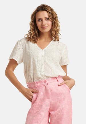 White short-sleeve blouse with eyelet detailing and a V-neck, paired with textured pink high-waisted trousers featuring front pockets.