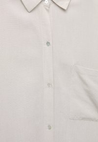 Chemise à boutons gris clair avec un col classique, petite poche et boutons en nacre. Texture lisse et tissée avec une finition subtile.