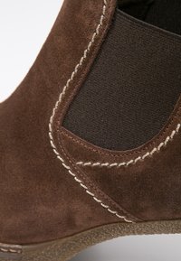 Bottine en daim marron avec panneau latéral élastique, surpiqûres blanches contrastantes et semelle en caoutchouc texturée.