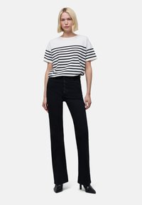 T-shirt noir et blanc à rayures associé à un pantalon noir taille haute avec des boutons visibles. Modèle portant des talons noirs.