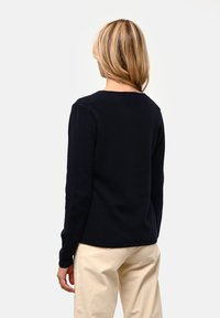 Námořnický modrý pletený svetr s dlouhými rukávy, kulatým výstřihem a hladkou strukturou. Zadní strana se vyznačuje jednoduchým, čistým designem a mírným zúžením na spodním okraji.