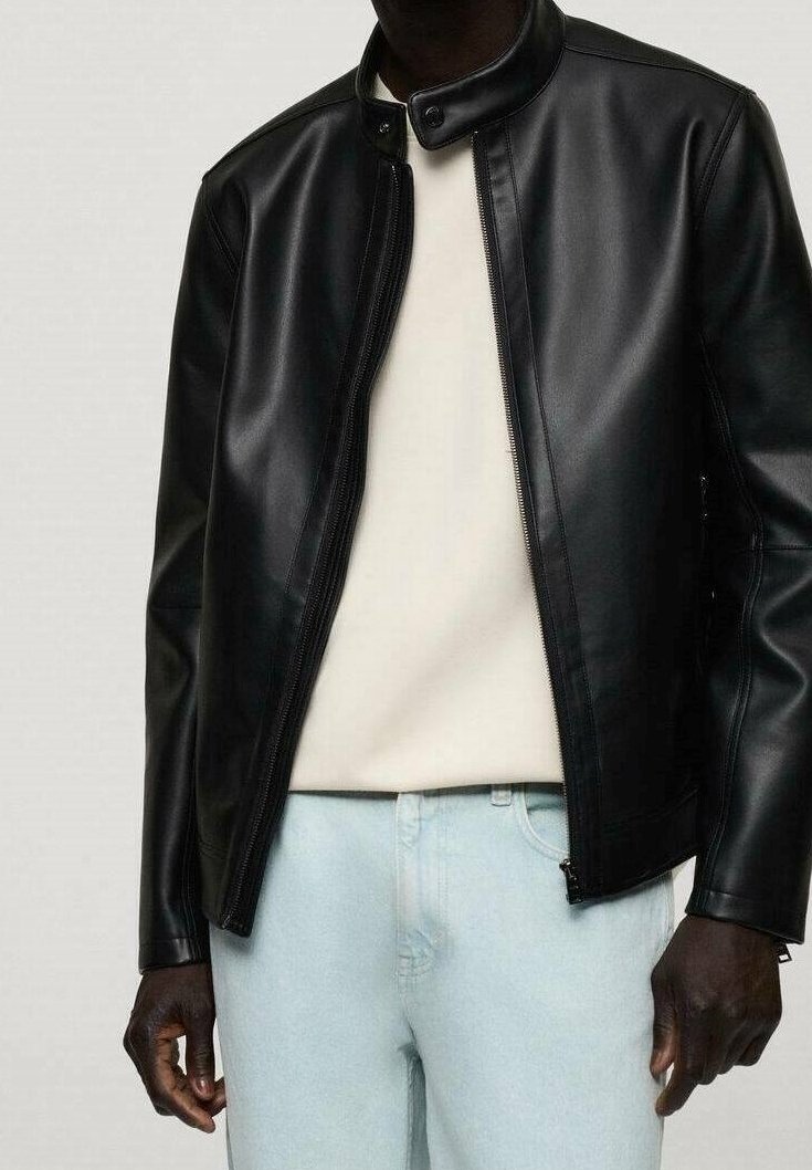 Veste en cuir synthétique noir avec col montant, fermeture à glissière à l'avant et texture lisse, associée à une chemise blanche et un jean clair.