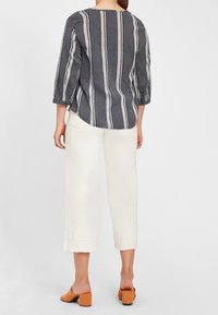 Granatowo-biała, w paski koszula z trzema ćwiartkami rękawów i zaokrąglonym dołem, zestawiona z białymi spodniami cropped i pomarańczowymi butami na słupku.