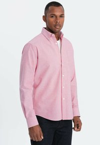 Vaaleanpunainen napillinen paita, jossa on kaulus, yksi rintatasku ja pitkät hihat, valmistettu teksturoidusta kankaasta. Paita on puettu valkoisen paidan päälle.