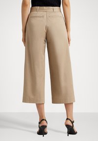 Beige wide-leg trousers made of cotton with a smooth texture, featuring two back pockets and a simple hemline, paired with black heeled sandals.