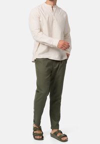 Vaaleanbeige pitkähihaisessa henley-paidassa on napitettava placket; yhdistetty oliivinvihreisiin puuvillahousuihin ja tummaan sandaaliin. Rennon istuvuuden ja yksinkertaisen muotoilun omaava asu.