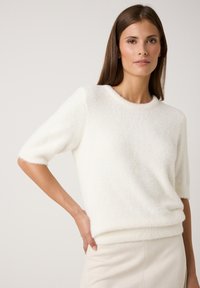 Weißer, plüschiger kurzärmeliger Pullover mit rundem Ausschnitt und weicher Textur, der an der Taille eng anliegt und dezente gerippte Akzente aufweist.