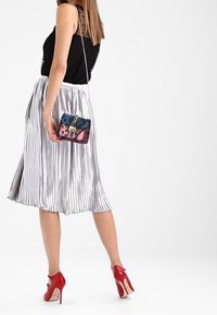 Gonna midi plissettata argento, top senza maniche nero, scarpe con tacco rosse e una borsa a tracolla colorata con una catena.