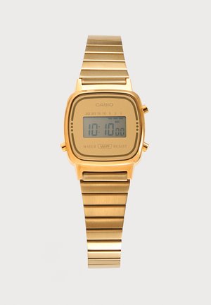 Χρυσό ψηφιακό ρολόι Casio με ορθογώνιο καντράν που δείχνει ώρα 10:10, μεταλλικό λουράκι και σήμανση αντοχής στο νερό.