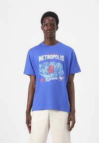 Blaue Baumwoll-T-Shirt mit einem grafischen Design einer Stadtansicht, dem Text "METROPOLIS", dem Superman-Logo und bunten Superhelden-Illustrationen.