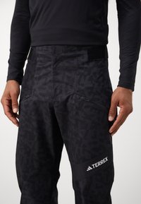 Μαύρο παντελόνι Terrex με υφή, τσέπες με φερμουάρ και ελαστική μέση. Στη χαμηλή πλευρά του ποδιού υπάρχει λευκό λογότυπο.