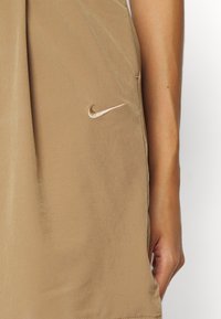 Hnědá sukně Nike s hladkým povrchem. Na přední straně se nachází malé vyšívané logo a má uvolněný siluetu.