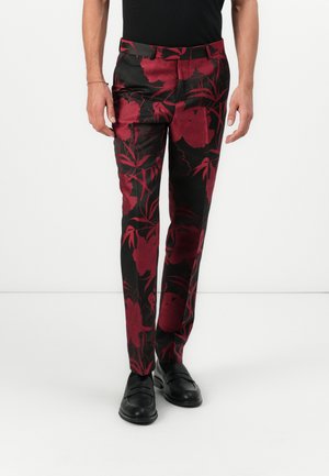 Schwarze Hosen mit einem roten Blumenmuster. Slim-Fit-Design mit einer glatten Textur; getragen mit schwarzen Loafers. Der Bund hat Gürtelschlaufen.
