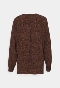 Blouse ample marron avec imprimé léopard noir. Dotée de manches longues et d'un col rond. Tissu doux et texturé. Dos uni.