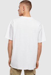 Camiseta de algodón blanca con mangas cortas, corte relajado, cuello redondo y una textura suave, presentada desde atrás sin diseño gráfico.