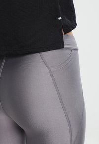 Czarny t-shirt z krótkim rękawem o lekkiej, oddychającej teksturze, zestawiony z szarymi dopasowanymi legginsami, które charakteryzują się gładkim materiałem i kieszeniami po bokach.