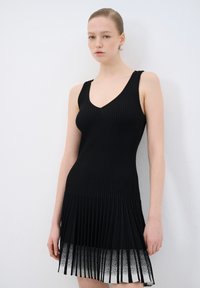 Abito in maglia a coste nera con scollatura a V, gonna svasata plissettata e effetto ombré che sfuma verso il bianco all'orlo.