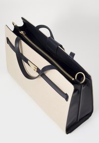 Beige canvas totebag met donkerblauwe leren accenten, voorzien van een ritssluiting, twee handvatten en een detail in goudkleurig metaal.