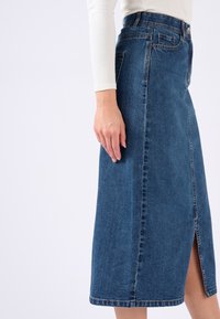 Denim-A-Linien-Rock in mittlerem Blau mit einem Frontschlitz, geradem Saum und klassischem Fünf-Taschen-Design. Der Stoff zeigt eine subtile Textur und Maserung.