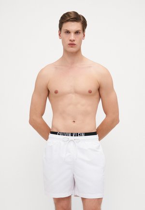 Shorts de bain blancs en tissu léger, dotés d'une taille élastique noire avec le logo "CALVIN KLEIN". Coupe droite, sans motifs.