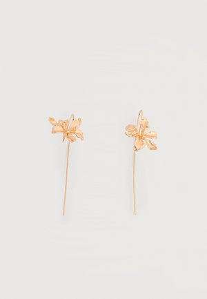 Boucles d'oreilles en métal doré en forme de fleurs délicates avec des tiges longues et fines et des fixations à crochet sur un fond uni.
