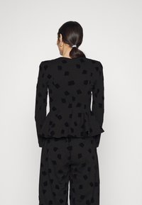 Černá sako s peplum efektem s texturovanými černými vzory listů, dlouhými rukávy a kulatým výstřihem, doplněné o odpovídající kalhoty.