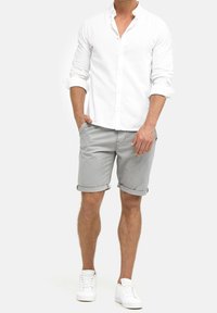 Biała koszula z guzikami, szare krótkie spodenki z podwiniętymi nogawkami i białe sneakersy. Cechuje się luźnym krojem, gładką fakturą i czystymi liniami.