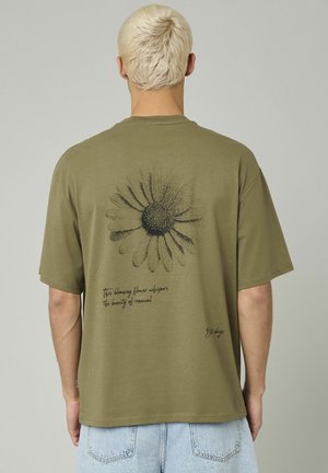 T-shirt en coton vert olive à manches courtes, avec un graphique de fleur noire et du texte dans le dos, coupe structurée et décontractée.
