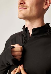 Schwarzer Quarter-Zip-Pullover aus weichem, dehnbarem Stoff; mit hohem Kragen und langen Ärmeln mit Daumenlöchern.