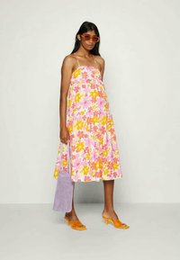 Vestido de verão floral com flores rosa e amarelas, alças nos ombros e uma saia rodada. Combinado com sapatos de salto laranja e uma bolsa de ombro lavanda.