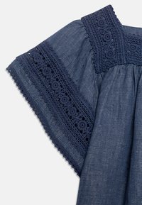 Marinblå ärm med blommig spetsdetalj och rynkad tygdetalj, som visar upp texturerad och dekorativ sömnad på en slät bakgrund.