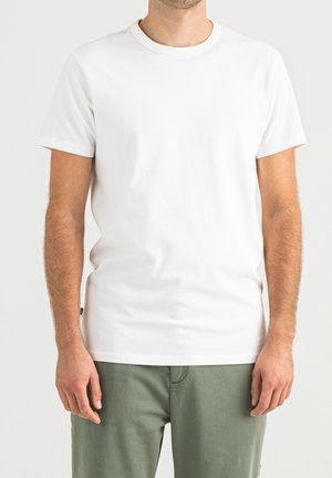 White cotton t-shirt with a round neck and short sleeves, featuring a plain design. Worn with green pants, showcasing a simple casual look.