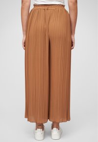 Brown pleated wide-leg pants with a textured fabric, elastic waistband, and white sneakers, viewed from the back.