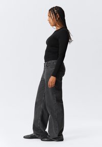 Un haut noir à manches longues associé à un jean gris foncé ample. Le jean présente une texture subtile et une taille standard.