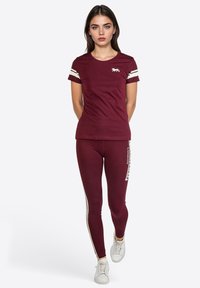 Camiseta burdeos con rayas blancas en las mangas y logo de león; leggings a juego con rayas laterales y texto; combinados con zapatillas blancas.