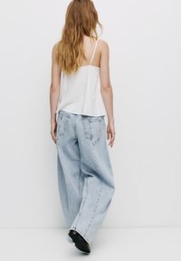 Witte mouwloze top met een relaxte pasvorm, gecombineerd met lichtblauwe wijde jeans met achterzakken en een vervaagde afwerking.