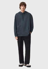 Tmavě modrý svetr s kapucí, přední kapsou, přitahovací šňůrkou a malým logem. V kombinaci s černými kalhotami a světlými teniskami s tmavými podrážkami.