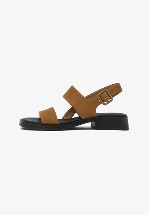 Brown suede sandal with two wide straps, adjustable buckle, black cushioned sole, and low block heel, side view on white background.