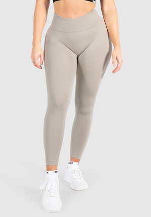 Lichtgrijze high-waisted leggings met een geribbeld patroon, voorzien van een soepele tailleband en een aansluitend ontwerp. Gecombineerd met witte sportschoenen.