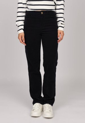 Pantalons en velours côtelé noirs à jambe droite avec une taille haute et des poches avant, associés à des baskets blanches. Texture à côtes verticales.